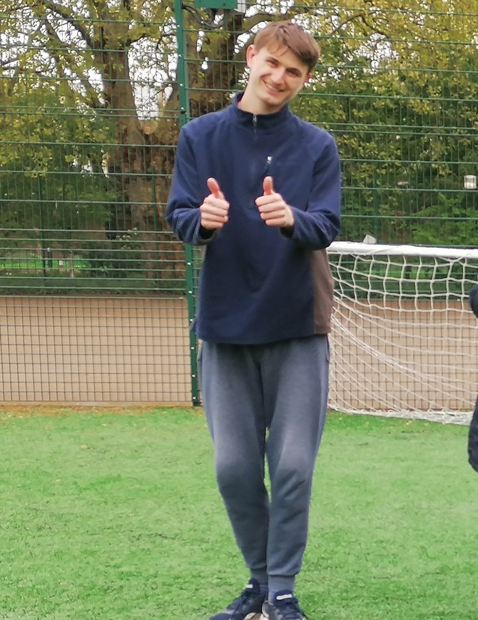 A man wearing a blue jumper smiles at the camera while giving two thumbs up.