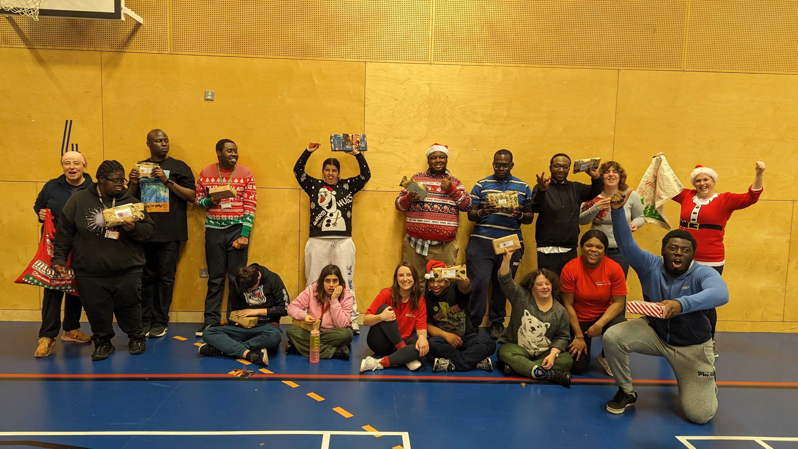 A group of people at a sports club smile and cheer at the camera whilst holding Christmas presents.