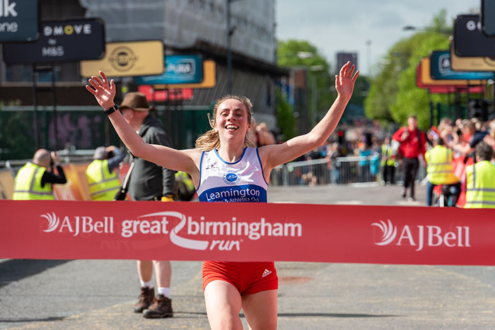 A woman smiles and raises her hands as she runs towards the finishing line at the Great Birmingham Run.